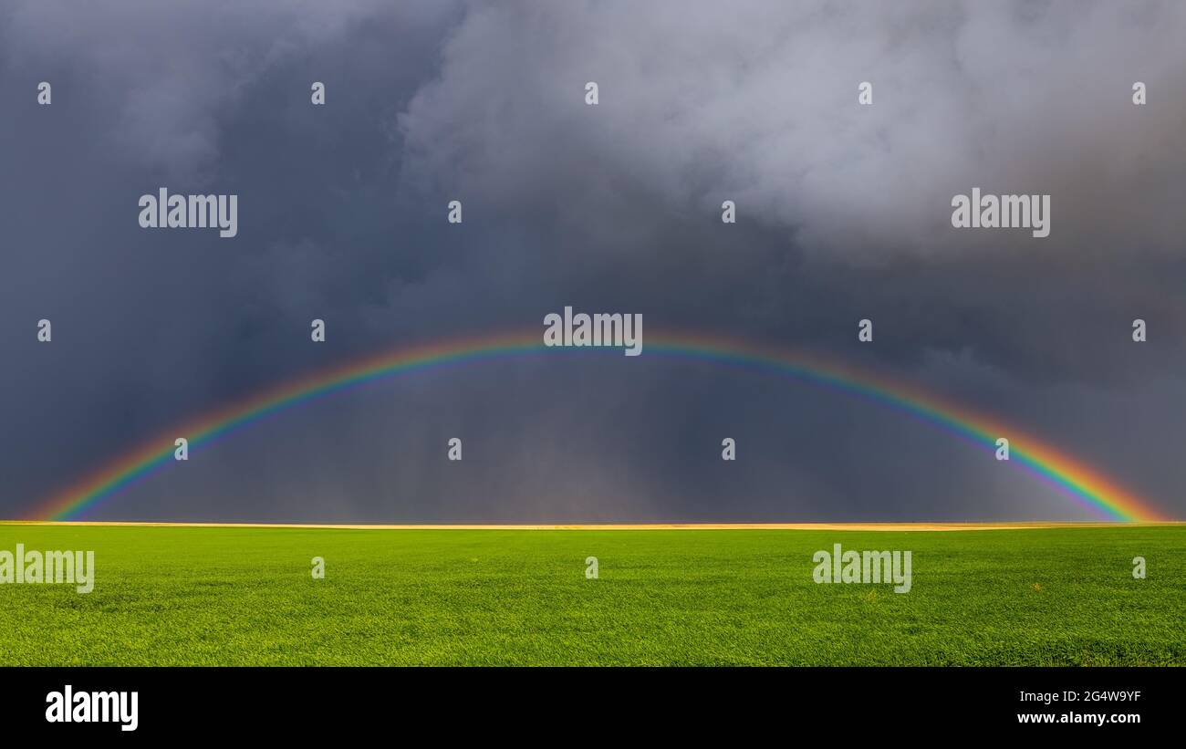 Il brillante arcobaleno splende sotto le nuvole buie della tempesta dopo violente tempeste e tornado che passarono attraverso le pianure orientali del Colorado. Foto Stock