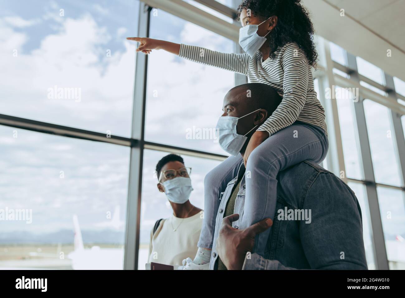 Famiglia che va a bordo del loro volo all'aeroporto durante la pandemia. Figlia sulla spalla del padre e gli aeroplani di puntamento mentre vanno con la madre all'aria Foto Stock