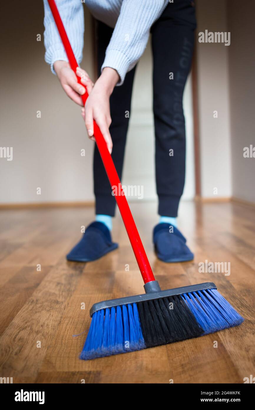 Giovane donna che pulisce un pavimento di legno con una spazzola di pulizia Foto Stock