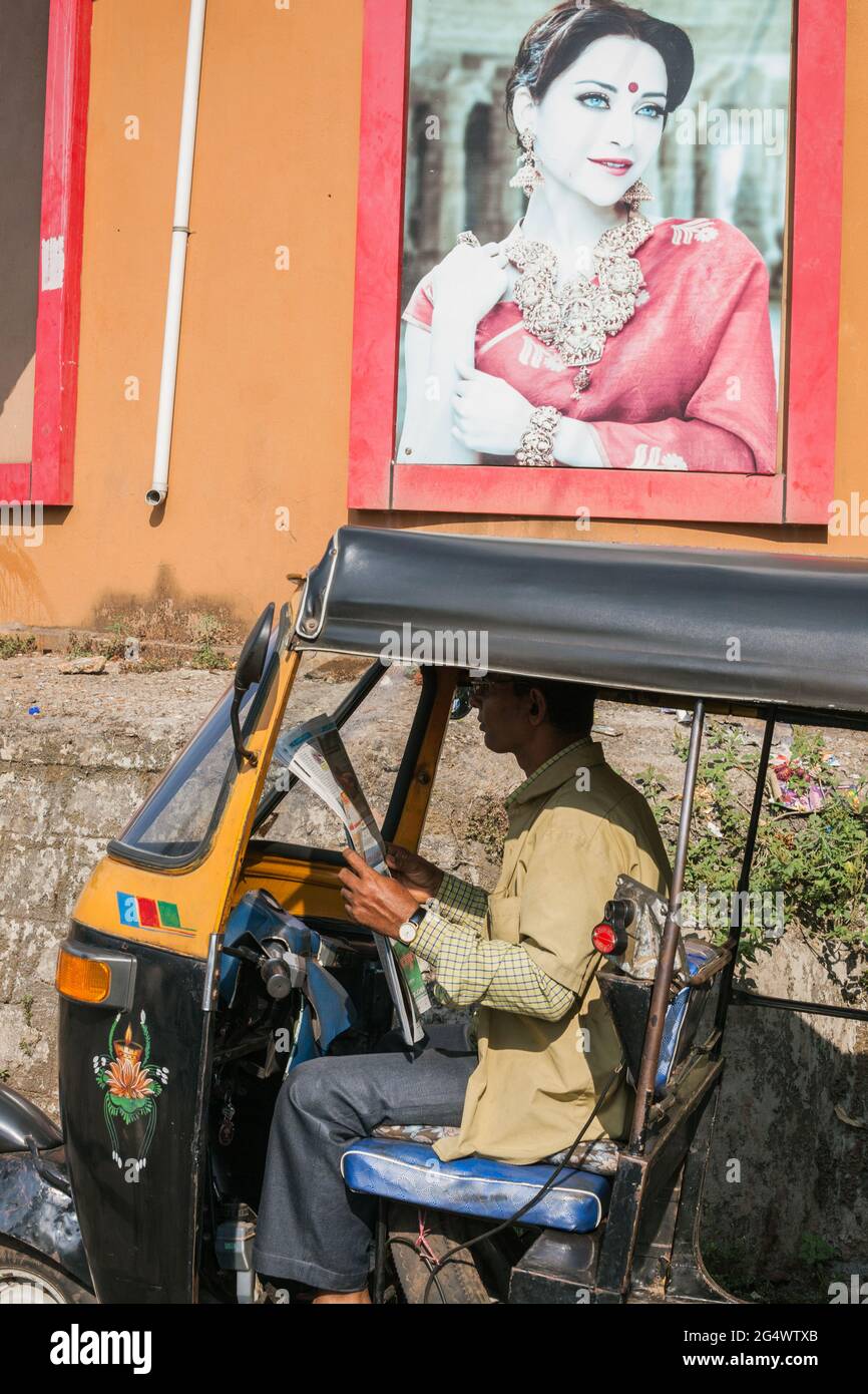 Il conducente indiano in risciò auto con divisa khaki si trova nel giornale di lettura in cabina, Udupi, Karnataka, India Foto Stock