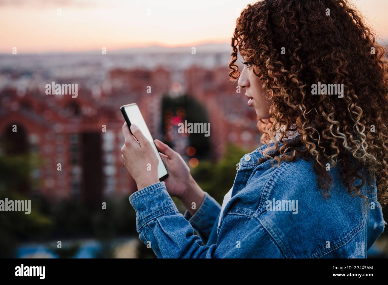 Donna ispanica che usa lo smartphone durante il tramonto Foto Stock