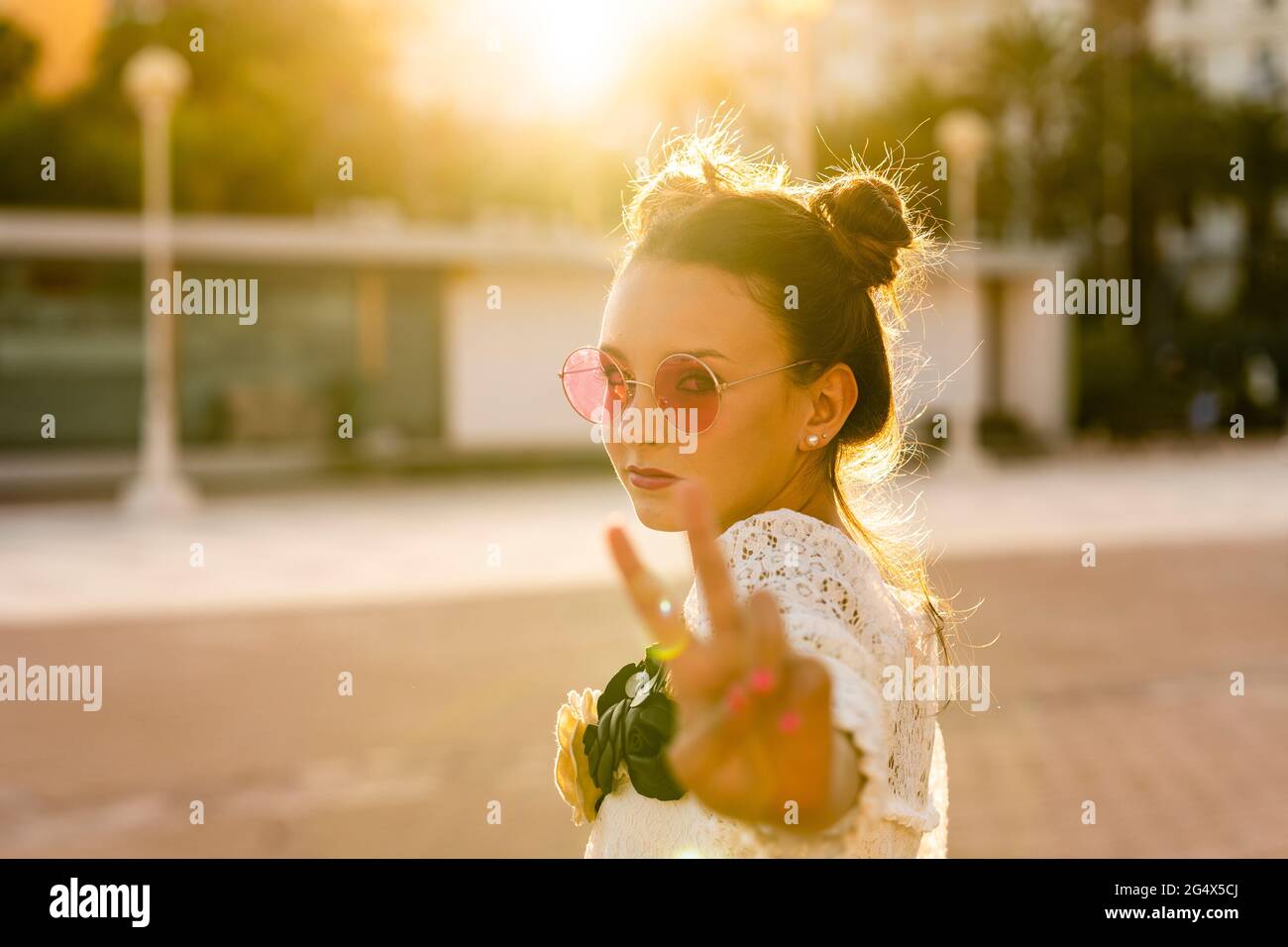 Ragazza adolescente che indossa occhiali da sole rossi mostrando segno di pace in città Foto Stock