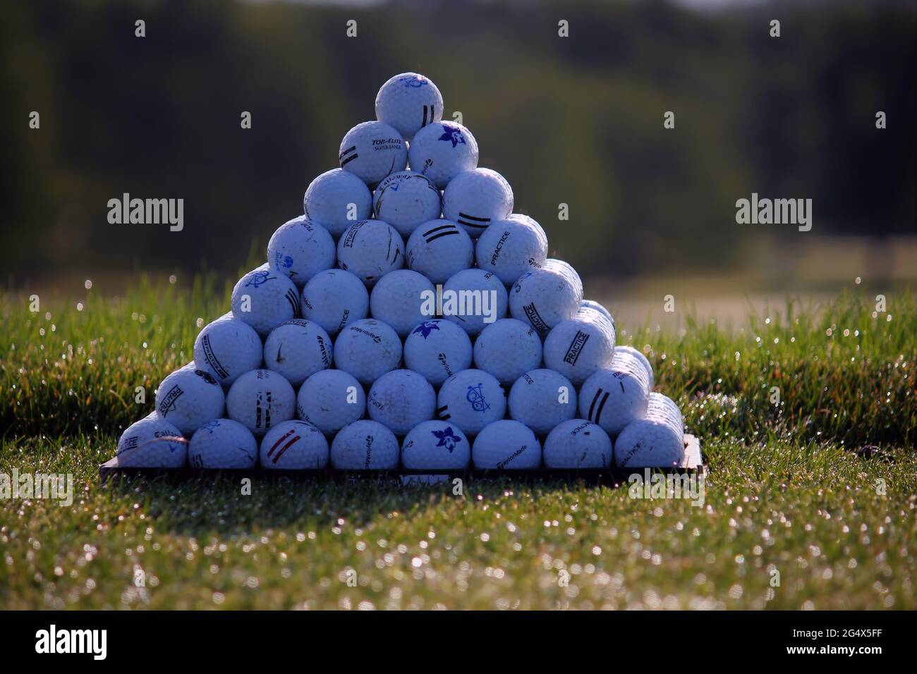 Una piramide solistica di palline da golf al mattino contro uno sfondo verde alberato Foto Stock