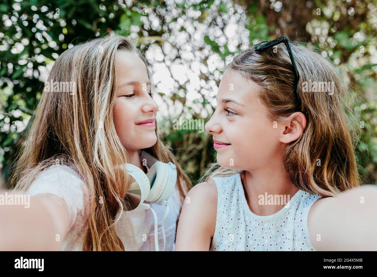 Sorridi le ragazze che si guardano l'un l'altro mentre prendono selfie in giardino Foto Stock