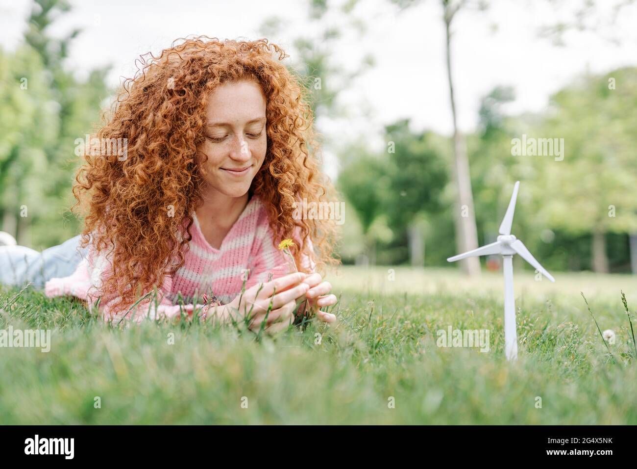 Giovane donna sorridente con capelli ricci distesi sull'erba al parco Foto Stock