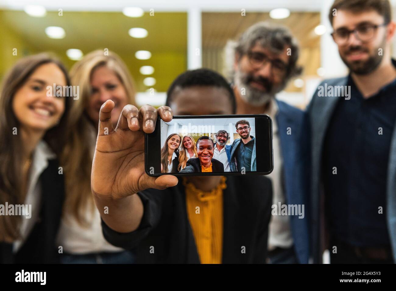 Donna d'affari sorridente che prende selfie attraverso il telefono cellulare con i colleghi di sesso maschile e femminile in ufficio Foto Stock