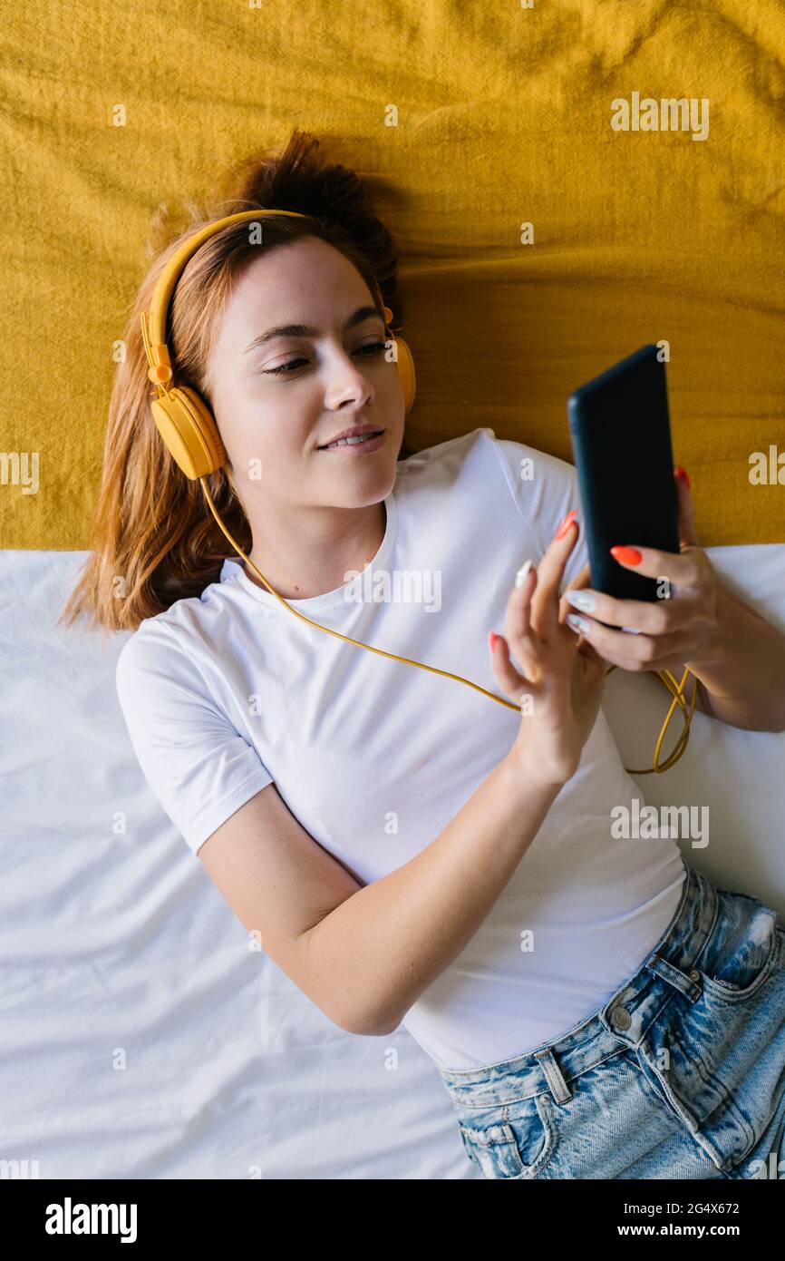 Donna sorridente sdraiata sulla schiena mentre ascolti la musica a casa Foto Stock