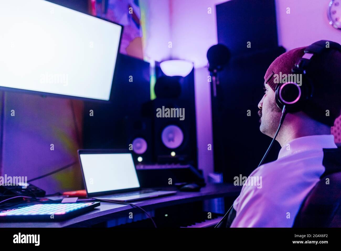 Uomo che indossa un cappello a maglia che guarda lo schermo del dispositivo mentre ascolti la musica in studio Foto Stock