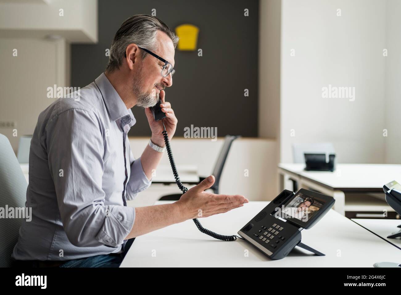 Imprenditore maschile che parla con un collega tramite telefono VoIP in ufficio Foto Stock