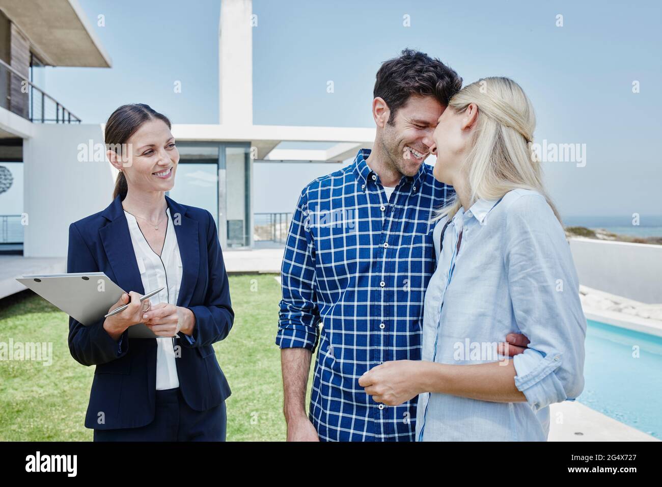 Agente immobiliare femminile sorridente mentre si trova in piedi da una coppia felice Foto Stock