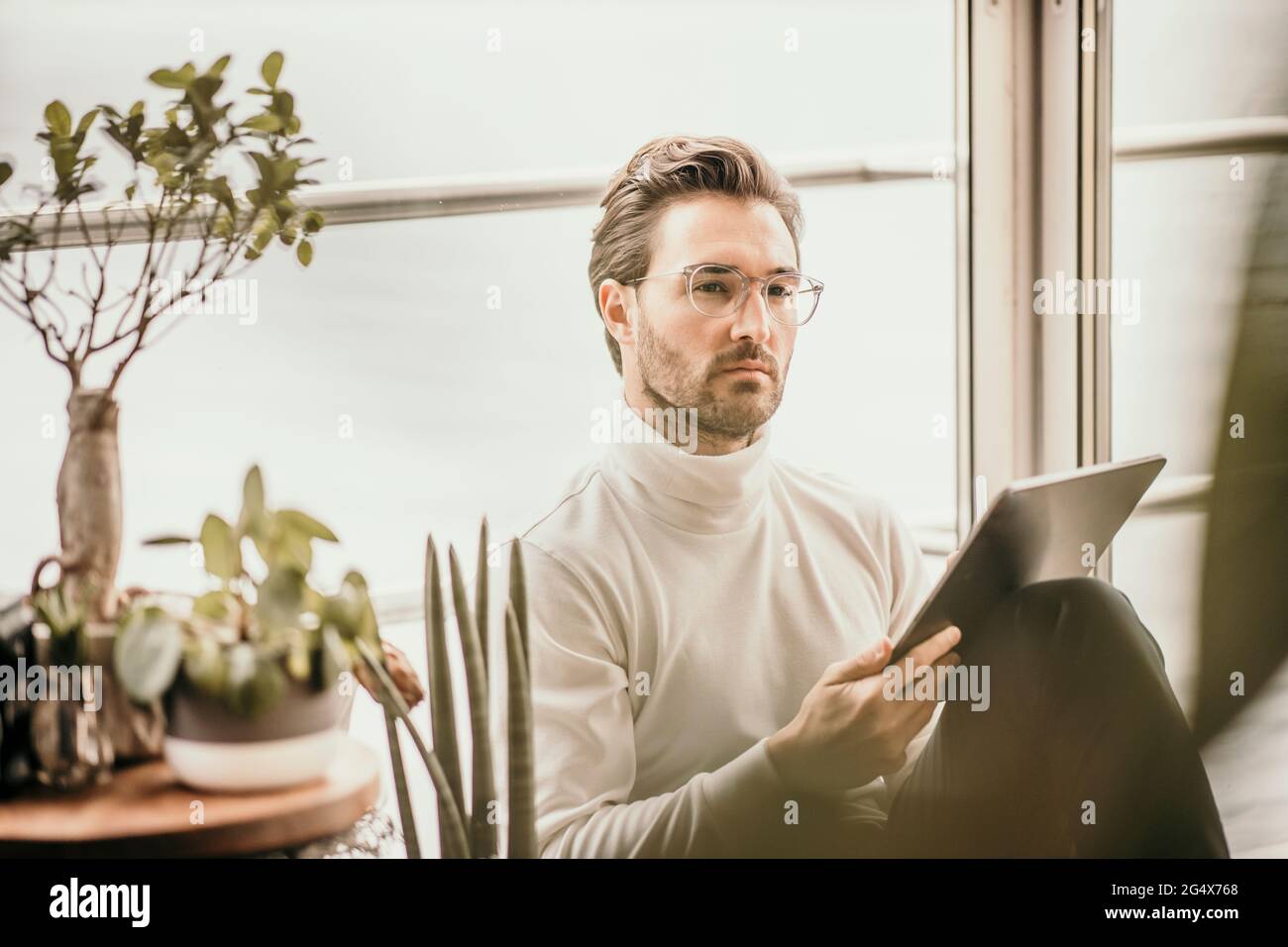 Uomo d'affari serio seduto con tablet digitale mentre contempla in casa galleggiante Foto Stock