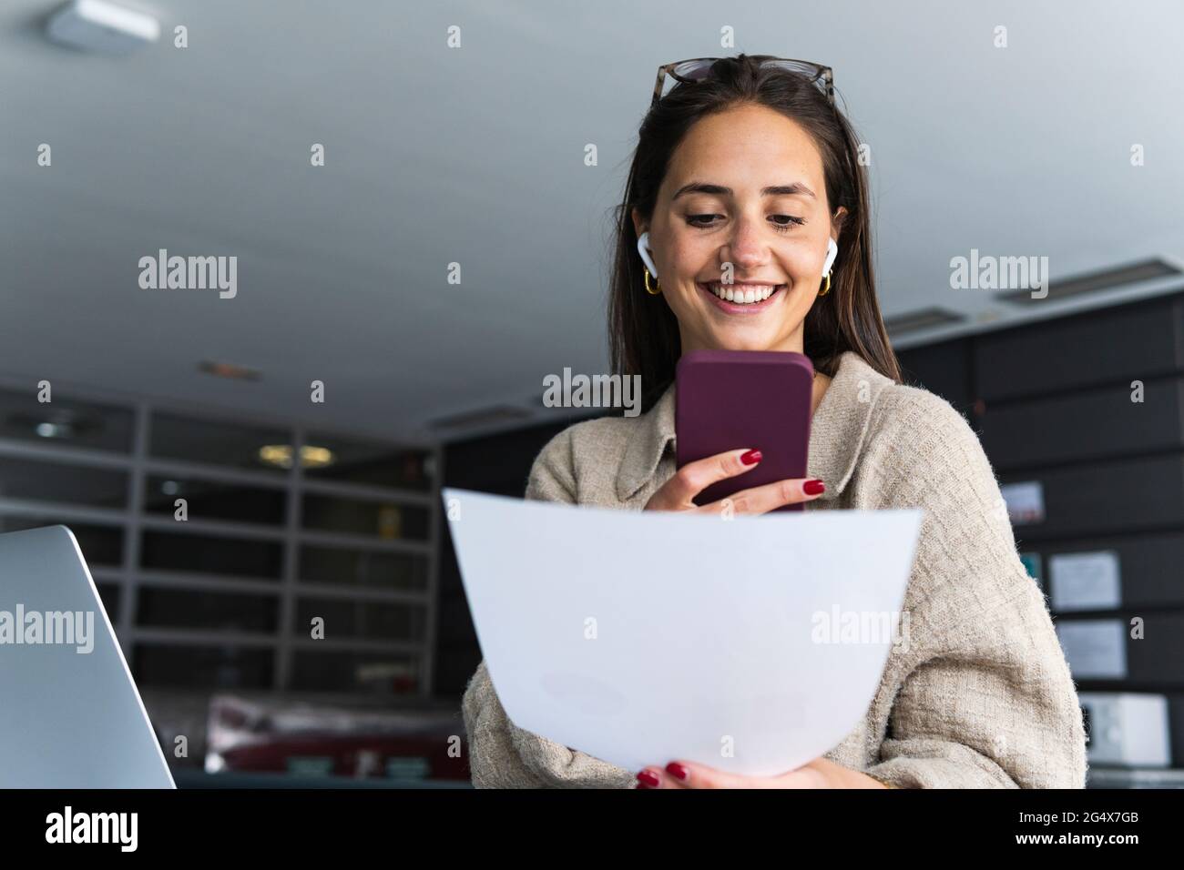 Sorridente giovane donna d'affari con invio di documenti Voicemail su smartphone in ufficio Foto Stock