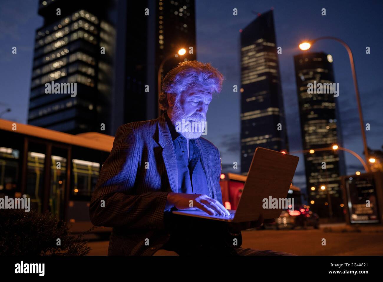 Uomo d'affari illuminato utilizzando un computer portatile in città di notte Foto Stock
