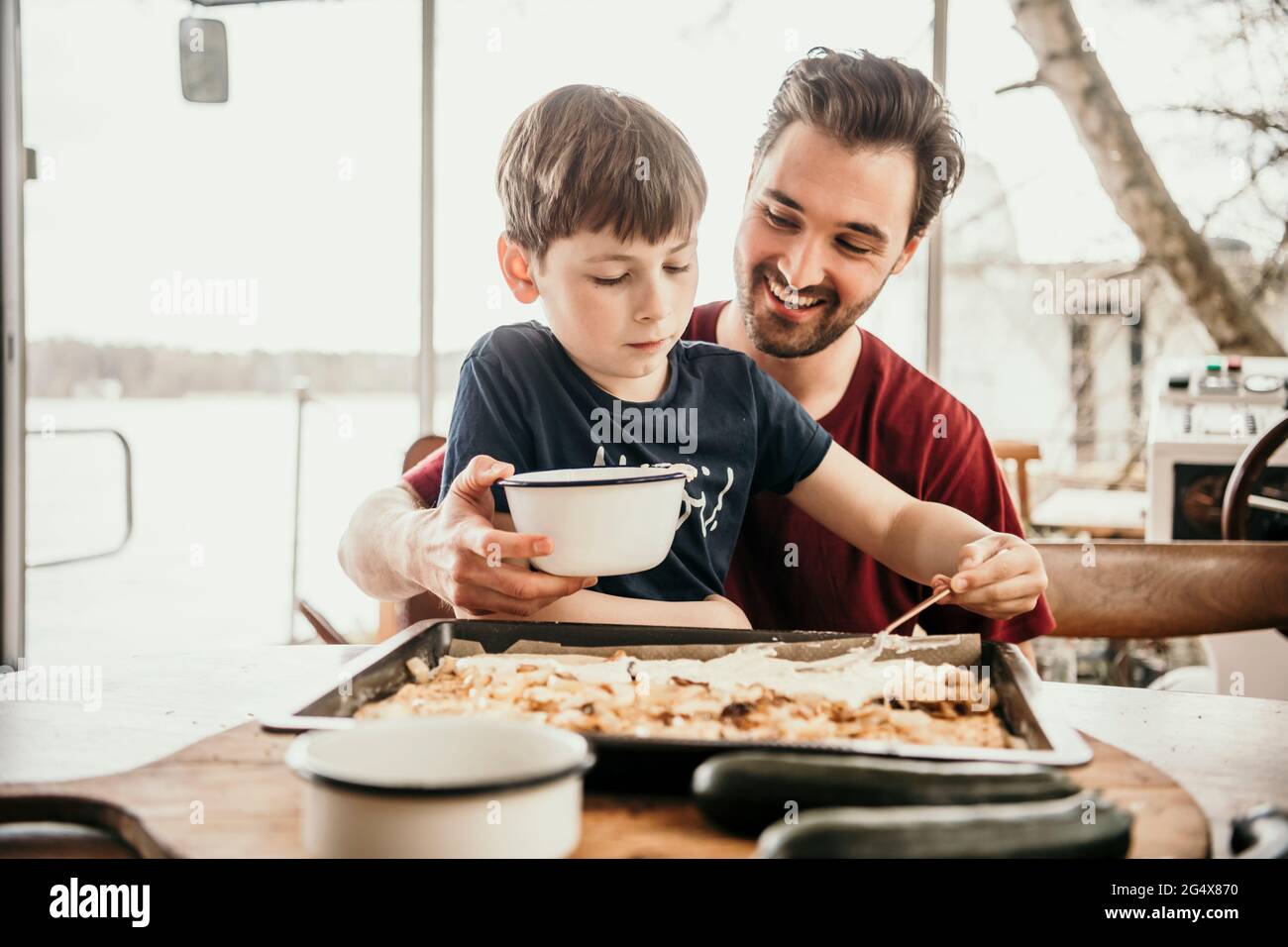 Sorridente padre che assiste il figlio nella preparazione del cibo a houseboat Foto Stock