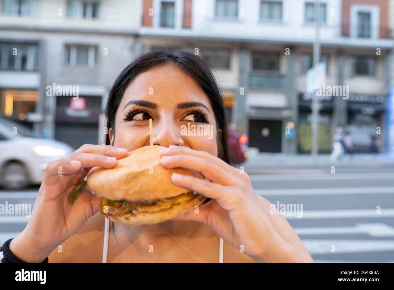 Giovane donna che mangia hamburger al bar sul marciapiede durante il tramonto Foto Stock