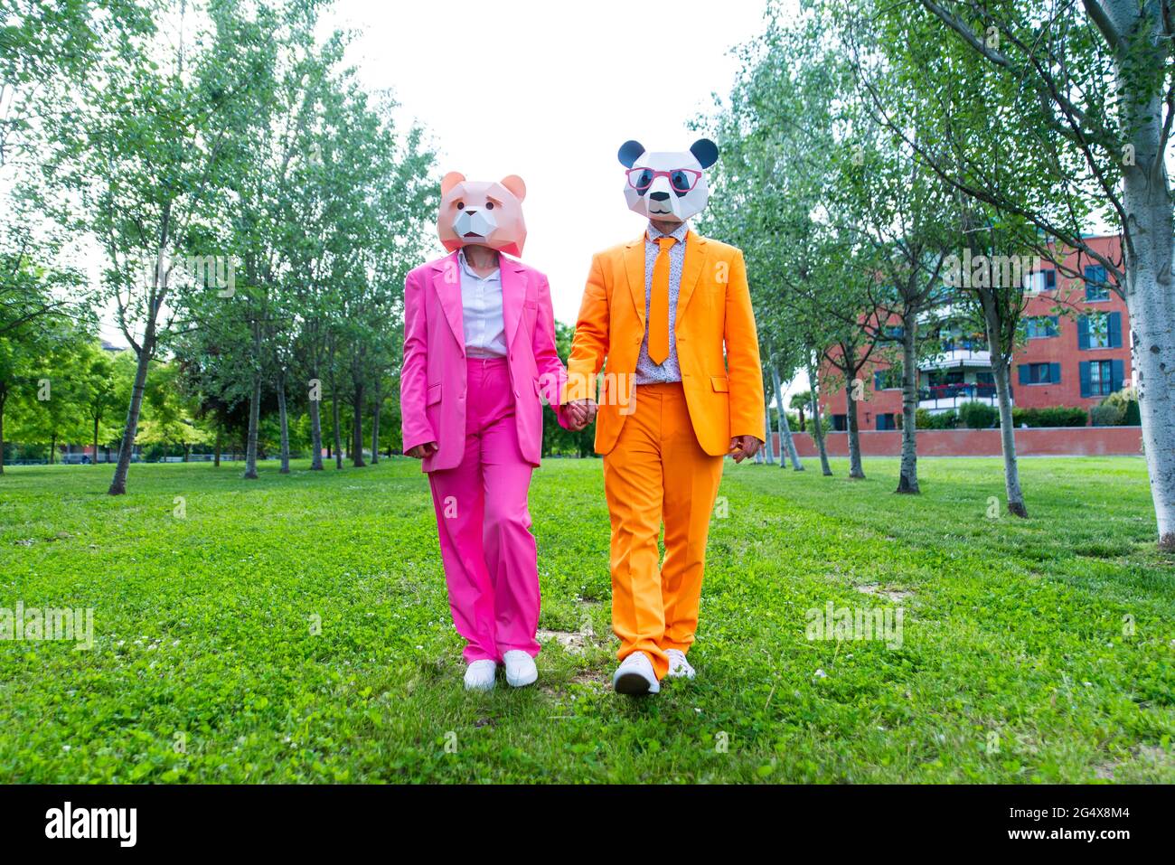 coupleÂ adulto indossa abiti vivaci e maschere animali che tengono le mani mentre cammina insieme nel parco verde Foto Stock