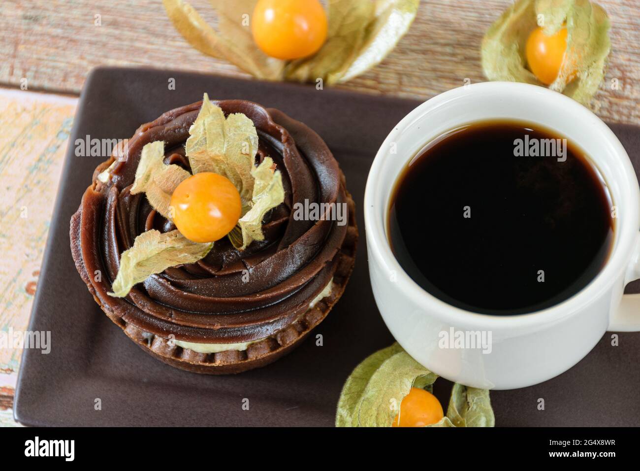 Closeup di mini torta con crema di mascarpone e ganache al cioccolato, decorato con fisico, accanto ad una tazza di caffè. Foto Stock