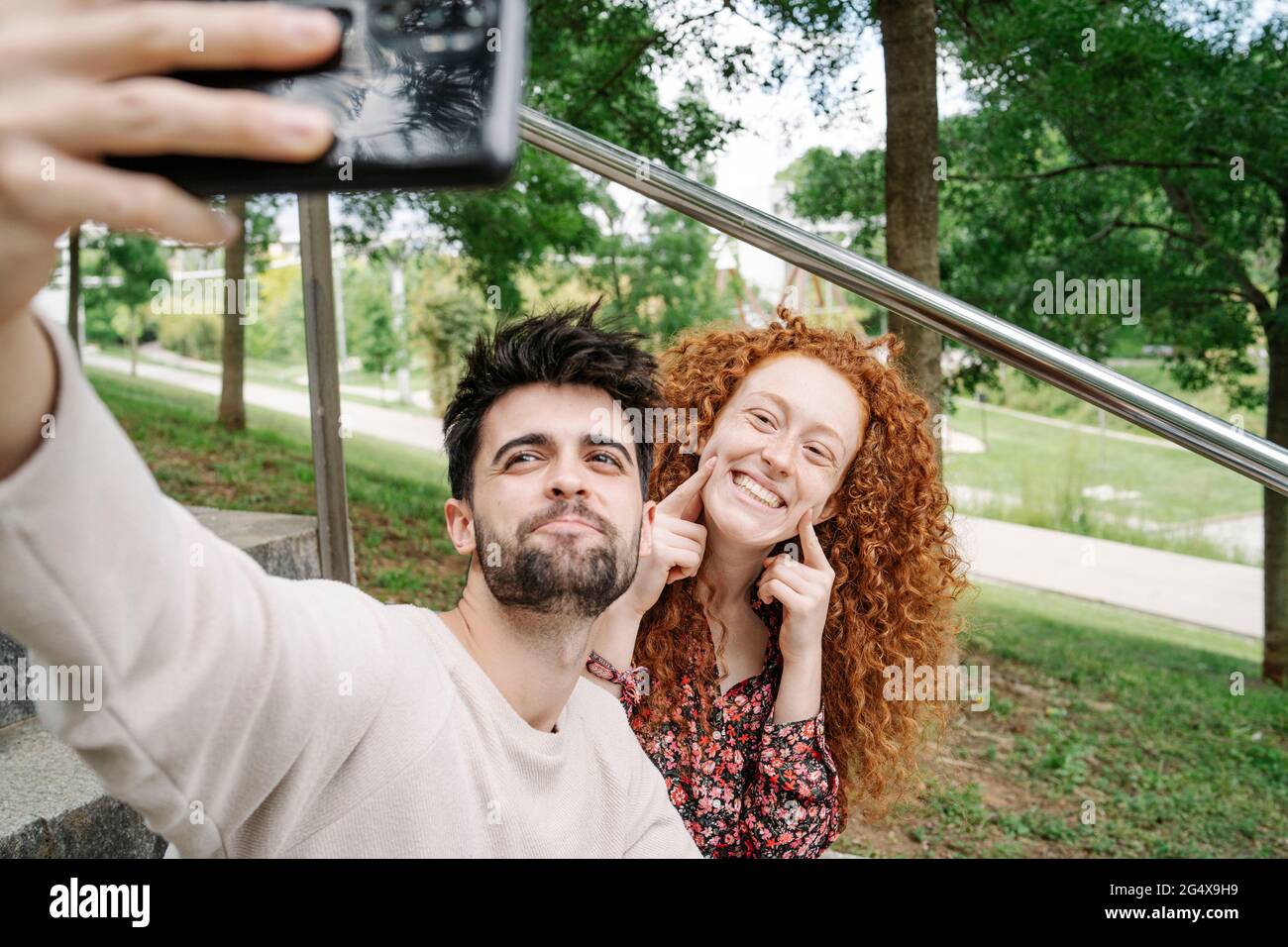 Giovane coppia che fa i volti carini mentre parla selfie nel parco pubblico Foto Stock