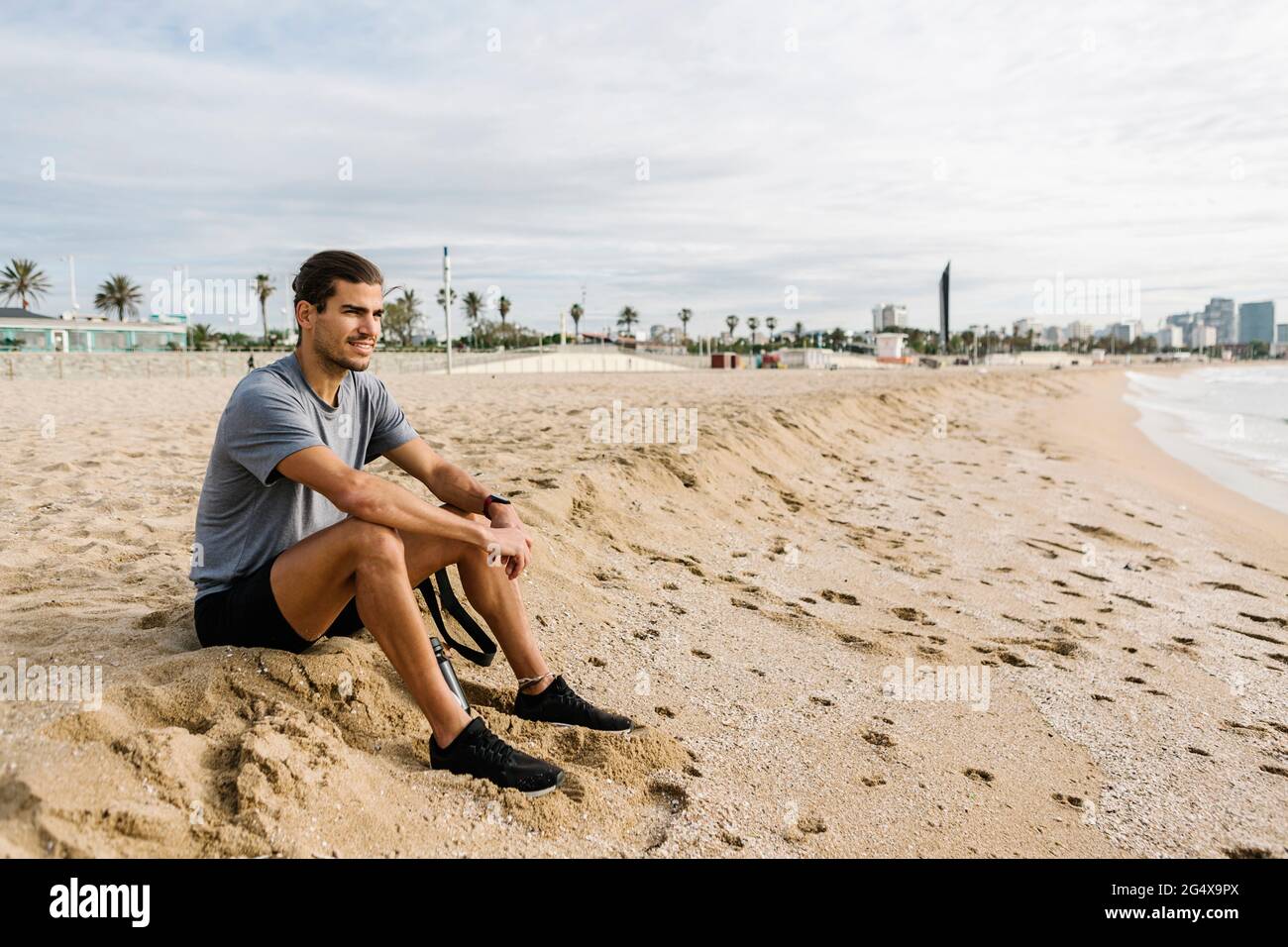 Atleta maschile guardando via mentre si siede sulla sabbia in spiaggia Foto Stock