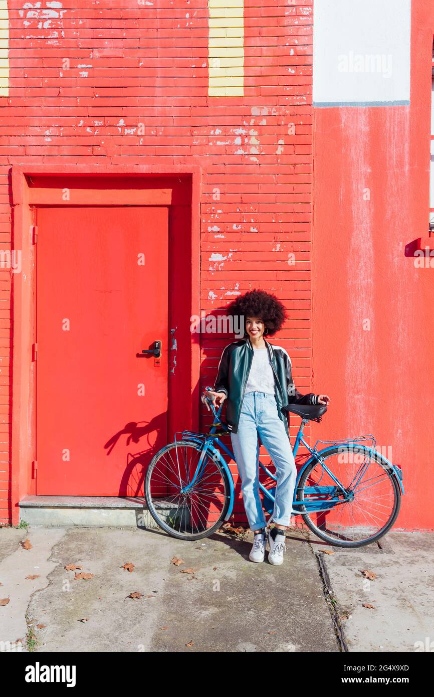 Giovane donna sorridente appoggiata in bicicletta davanti all'edificio rosso Foto Stock