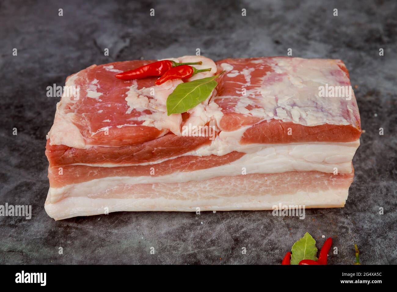 Pezzo rosso e bianco di pancia di maiale cruda con aglio su sfondo scuro. Foto Stock