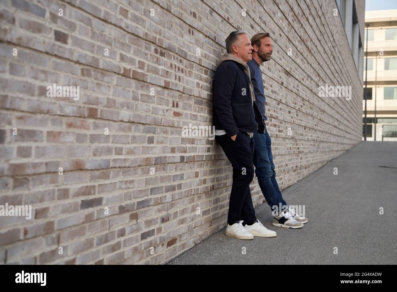 Uomini d'affari maturi che parlano l'uno con l'altro mentre si appoggiano sul muro Foto Stock