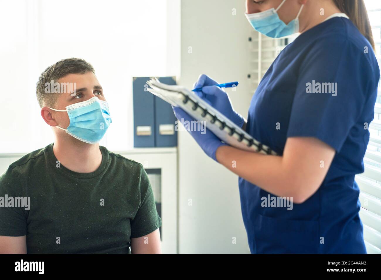 Medico femminile in maschera protettiva viso che prende intervista del paziente prima della vaccinazione in clinica Foto Stock