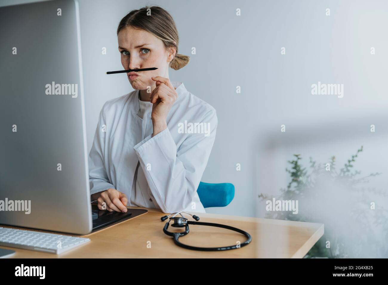 Donna medico che gioca con la penna mentre si siede alla scrivania Foto Stock