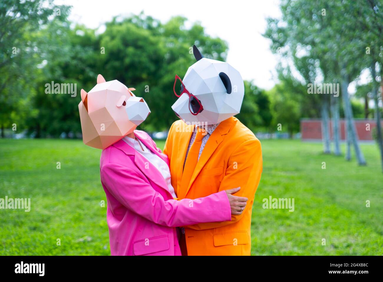 coupleÂ per adulti che indossa abiti vivaci e maschere animali che abbracciano il parco pubblico Foto Stock