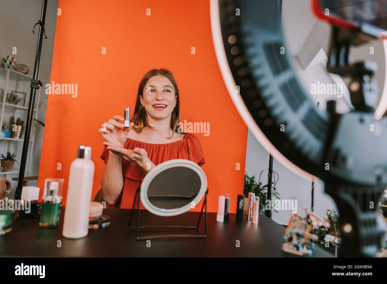 Sorridente influencer femminile che presenta rossetto durante il make-up tutorial filmare a casa Foto Stock