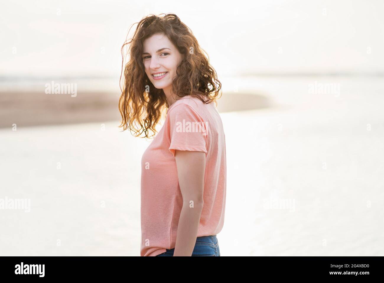 Bella donna che guarda sulle spalle mentre si è in piedi in spiaggia durante la giornata di sole Foto Stock