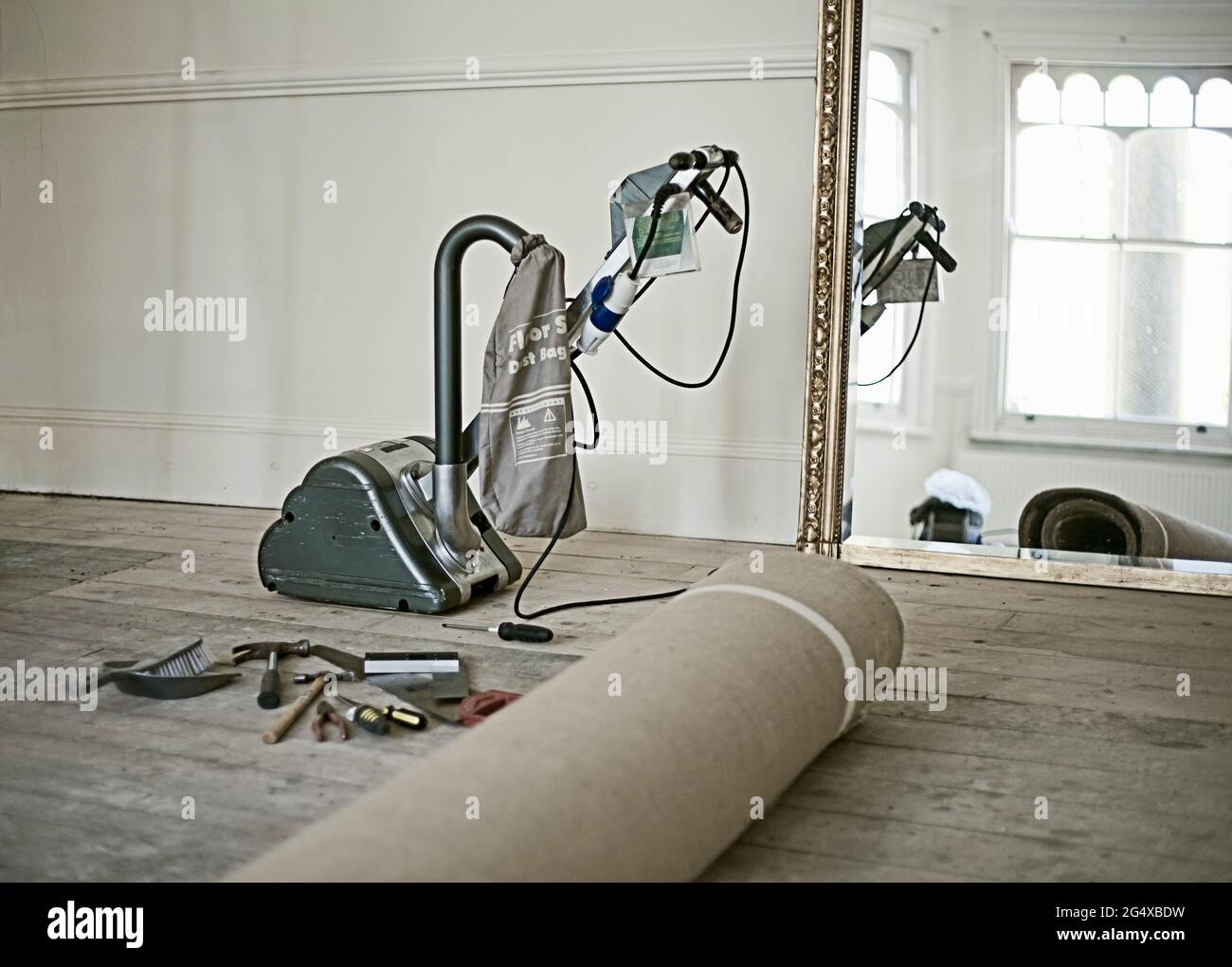 Moquette arrotolata, attrezzi da lavoro e levigatrice per pavimenti giacenti in un soggiorno vuoto Foto Stock