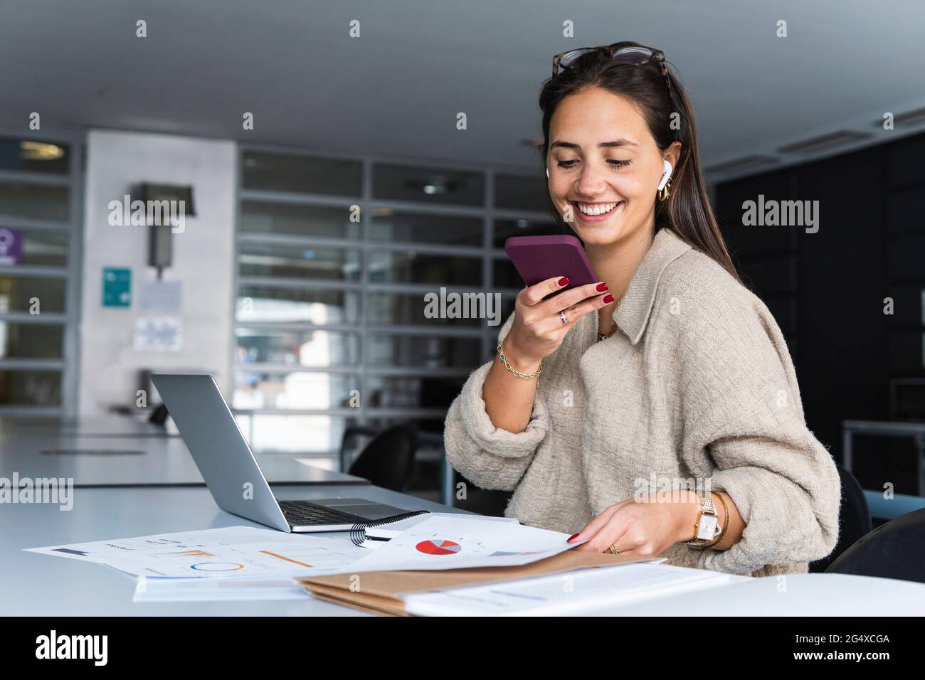 Donna d'affari sorridente che invia messaggi vocali tramite telefono cellulare in ufficio Foto Stock