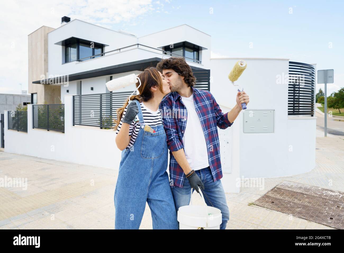 Coppia con rullo di vernice baciare di fronte a casa nuova Foto Stock