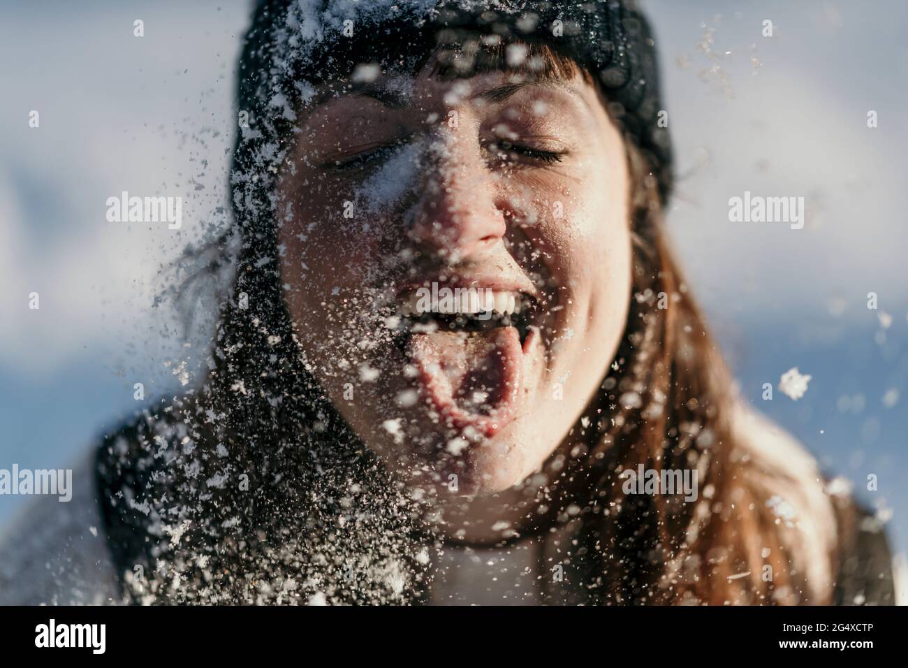 Donna mid adulta che esce dalla lingua mentre gioca durante la nevica Foto Stock