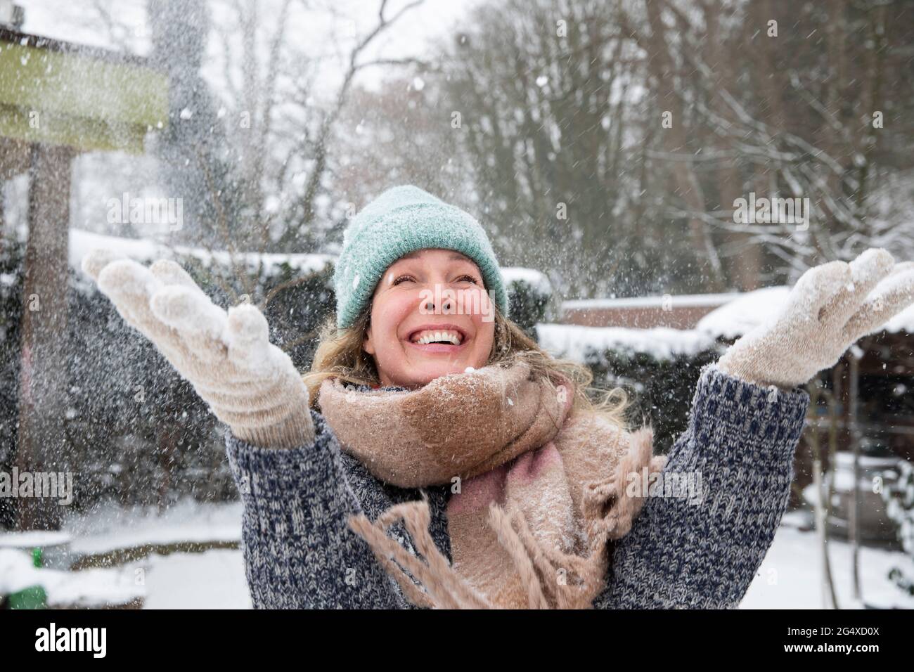 Giocosa donna matura che getta la neve in cortile durante l'inverno Foto Stock