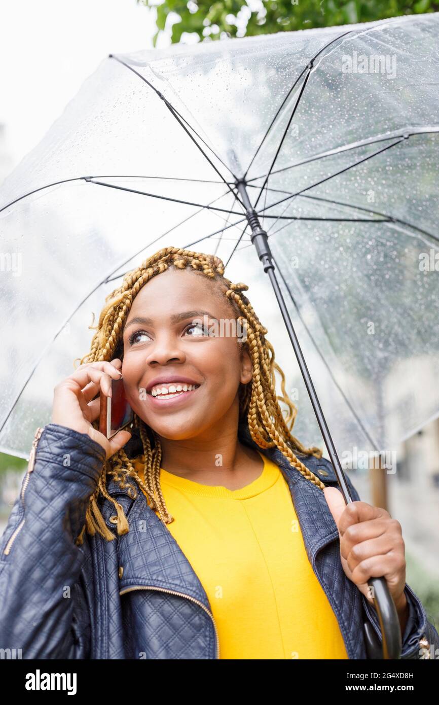 Donna sorridente che parla al telefono mentre tiene l'ombrello Foto Stock