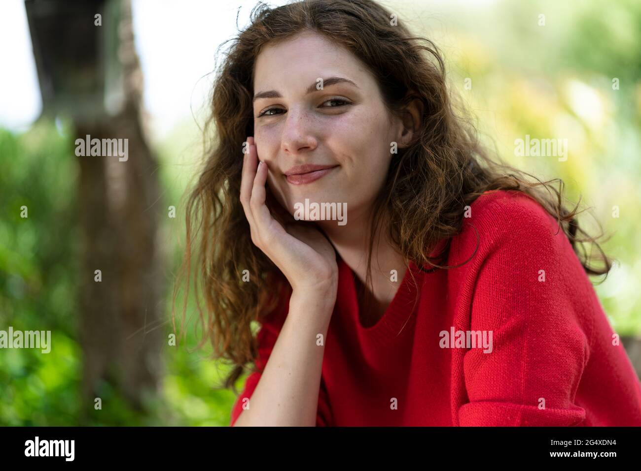 Donna sorridente con la mano sul mento in giardino Foto Stock