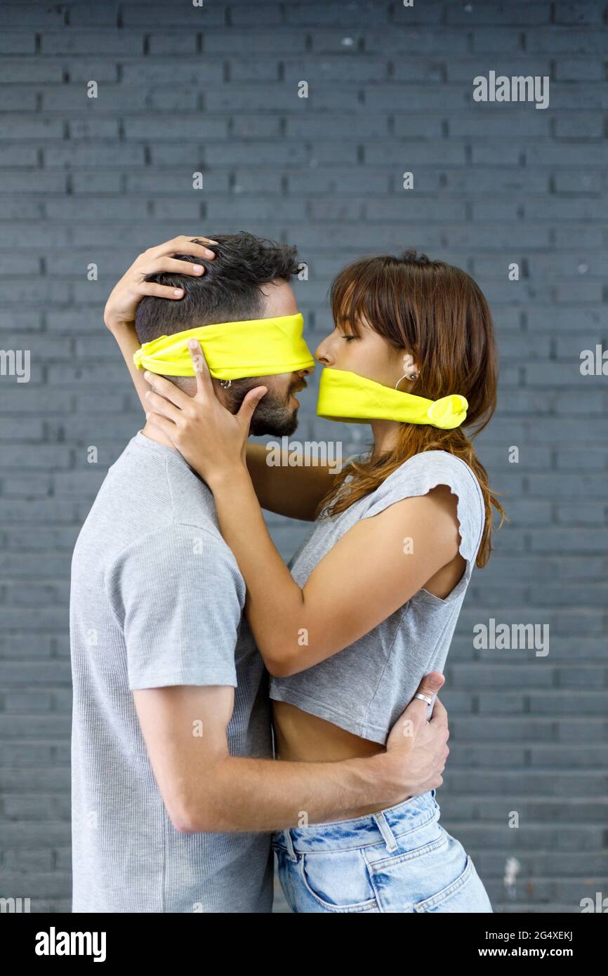 Accoppia con gli occhi e la bocca ricoperti di stoffa che fa romanticismo dalla parete grigia Foto Stock