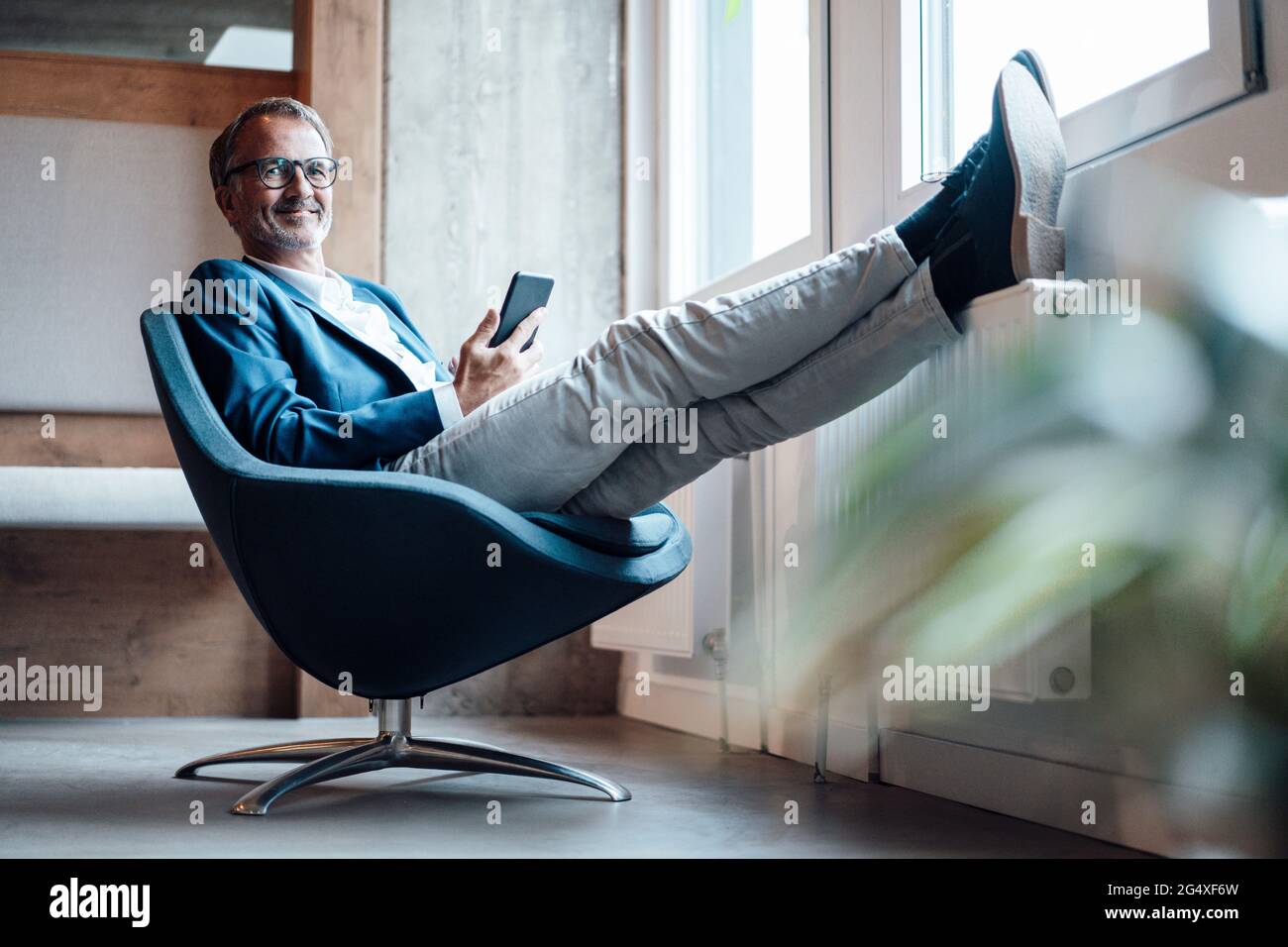 Uomo d'affari sorridente seduto con gambe incrociate alla caviglia in ufficio Foto Stock