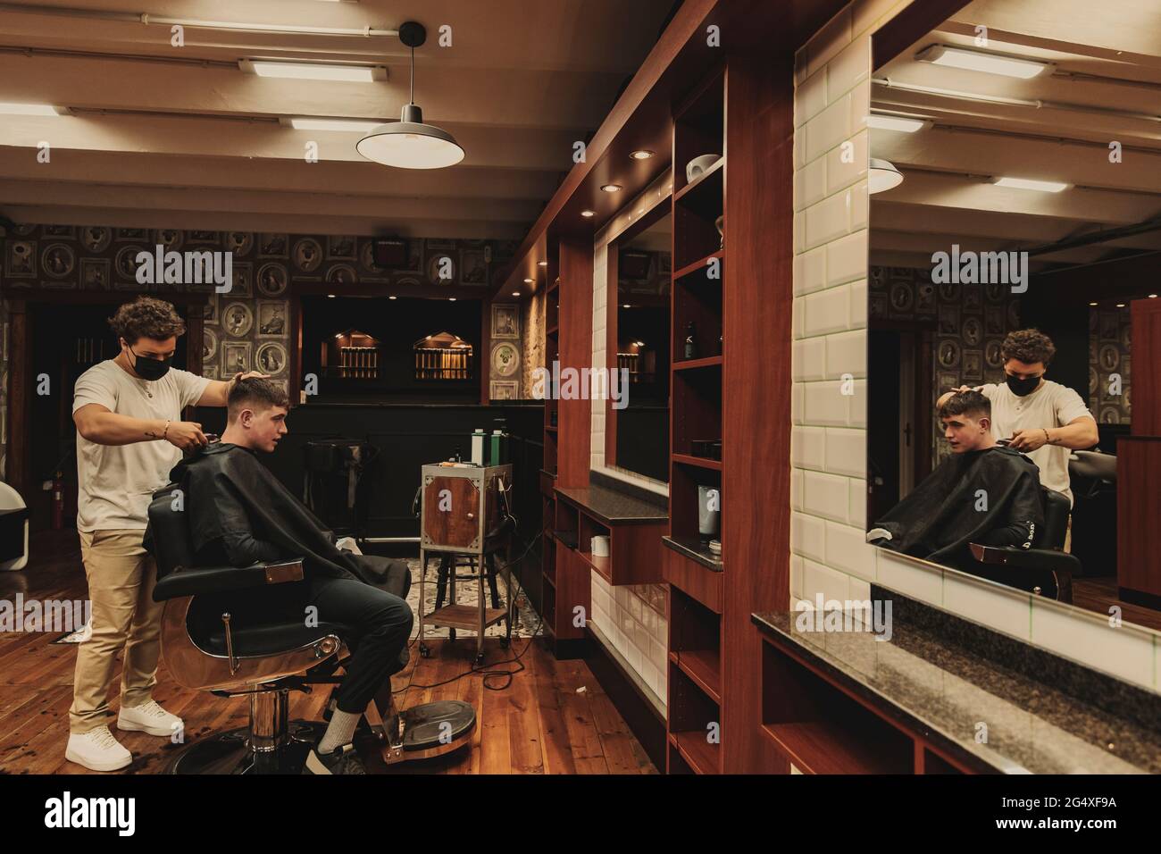 Giovane uomo che ottiene il taglio di capelli da barbiere maschio in salone durante la crisi COVID-19 Foto Stock