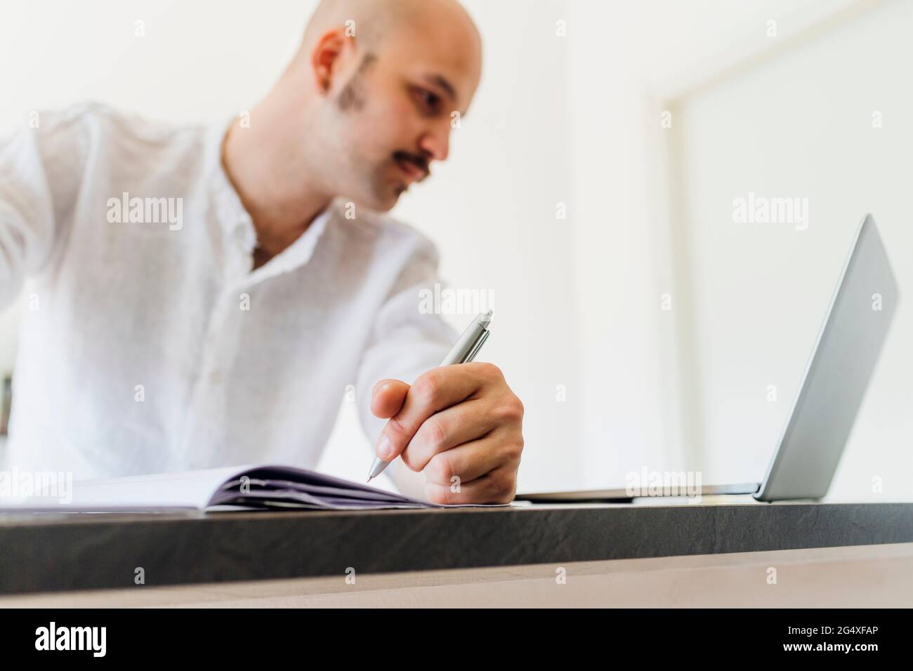 Giovane uomo con penna che guarda il computer portatile in cucina Foto Stock
