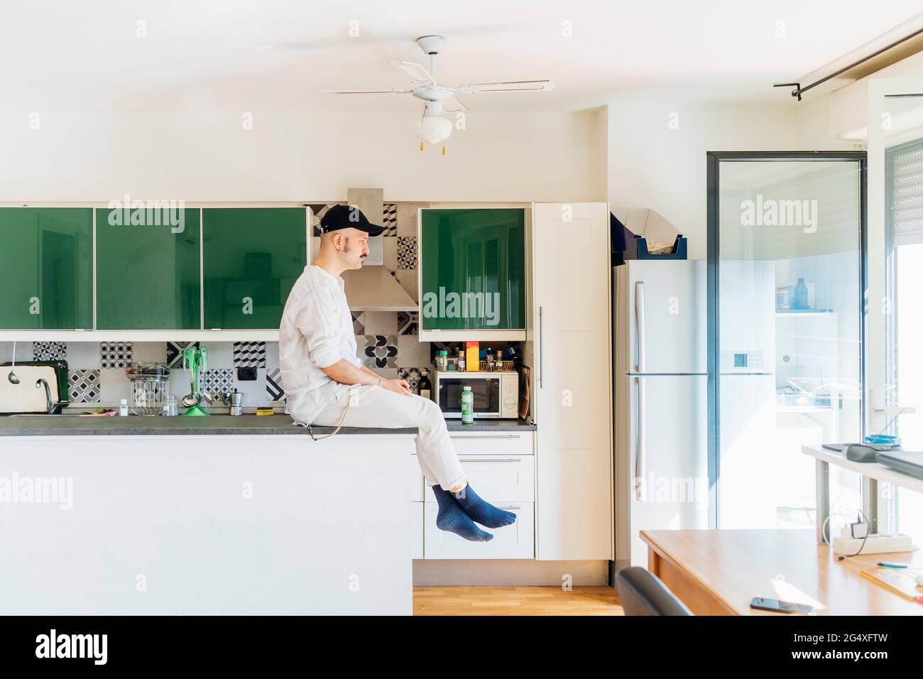 Giovane uomo che guarda via mentre si siede sull'isola della cucina a casa Foto Stock
