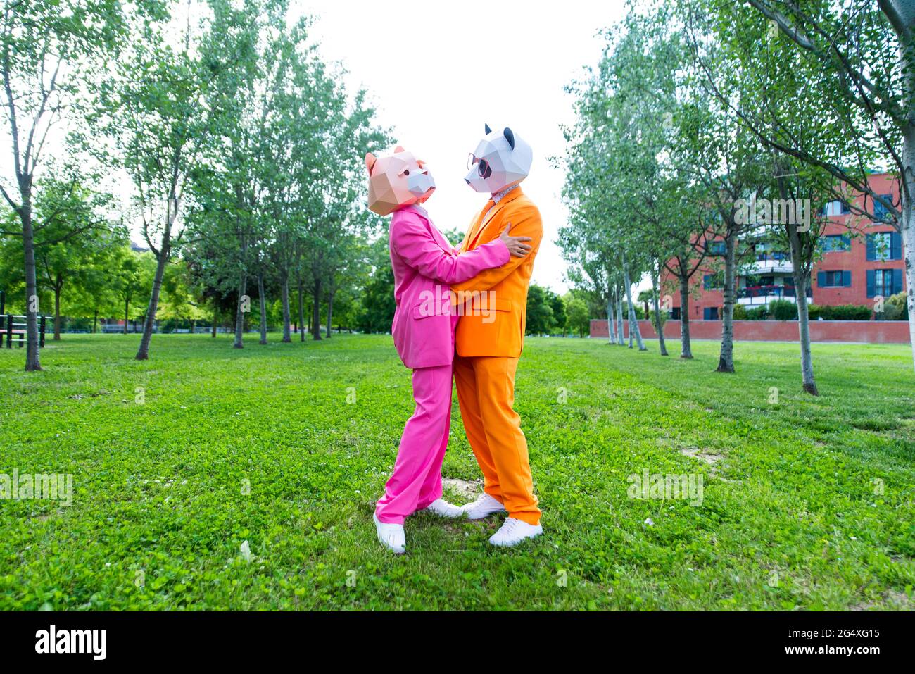 Adulto coupleÂ indossare abiti vivaci e maschere animali abbracciando nel parco verde Foto Stock
