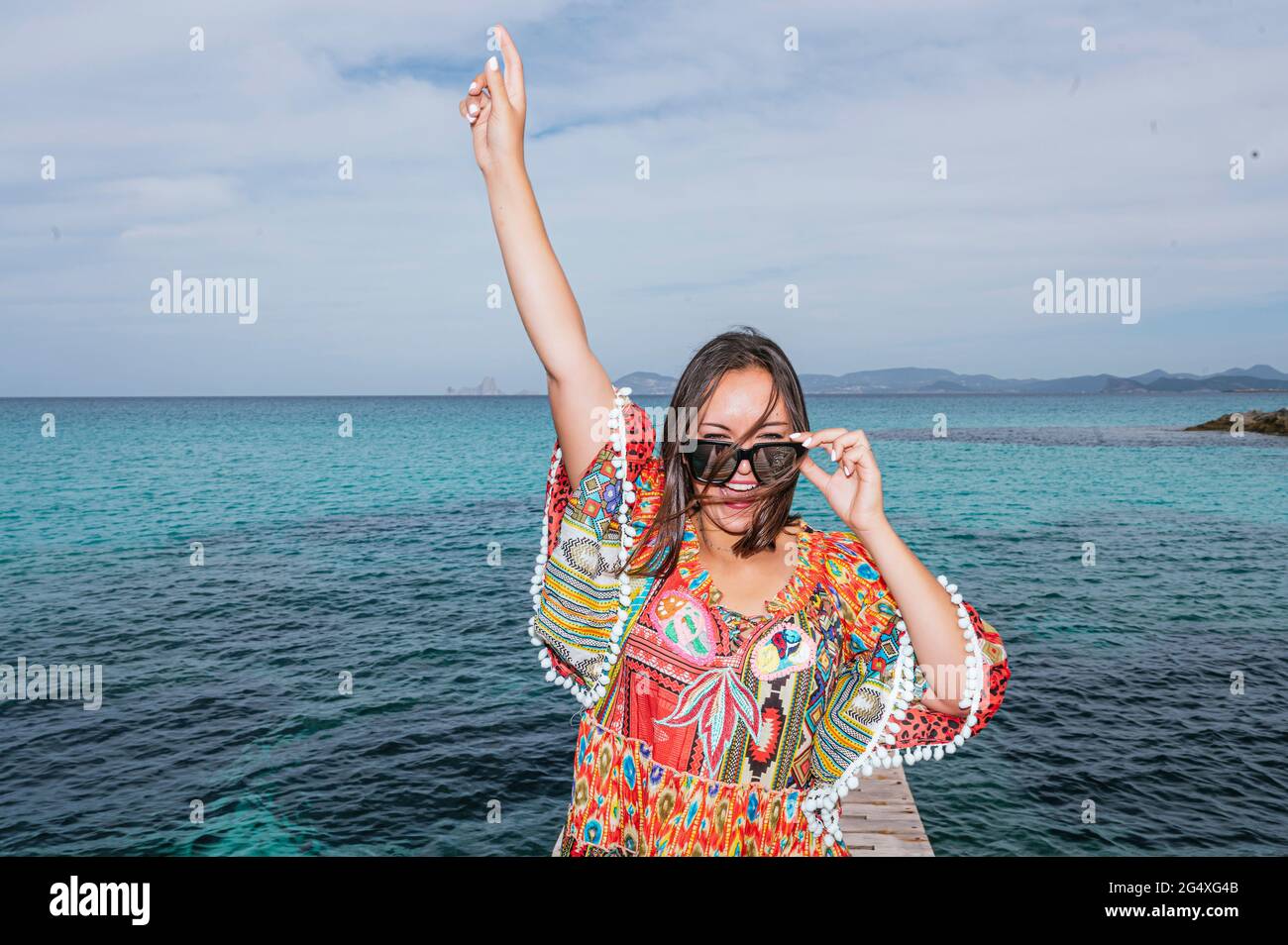 Donna allegra con la mano sollevata in piedi di fronte all'acqua sull'isola di Formentera Foto Stock
