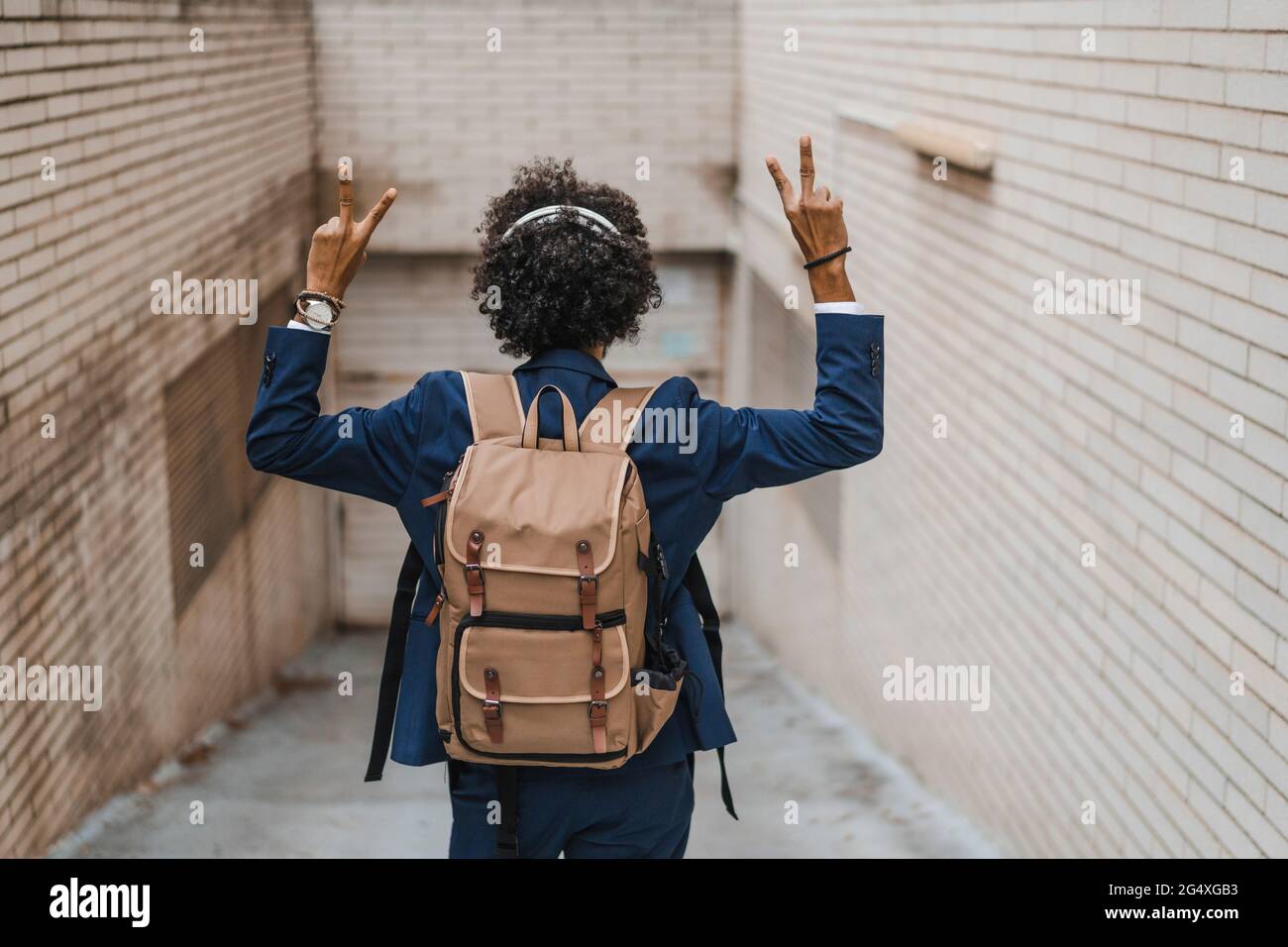 Imprenditore maschile con zaino gesturing segno di pace in piedi da muro Foto Stock