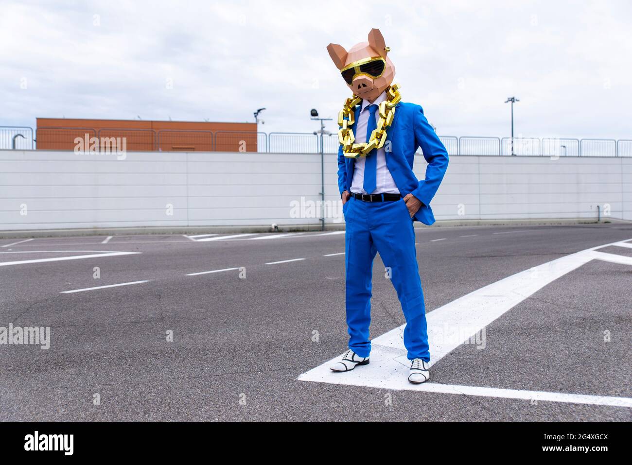 Personaggio divertente che indossa maschera animale e costume da lavoro blu divertendosi su un parcheggio vuoto Foto Stock
