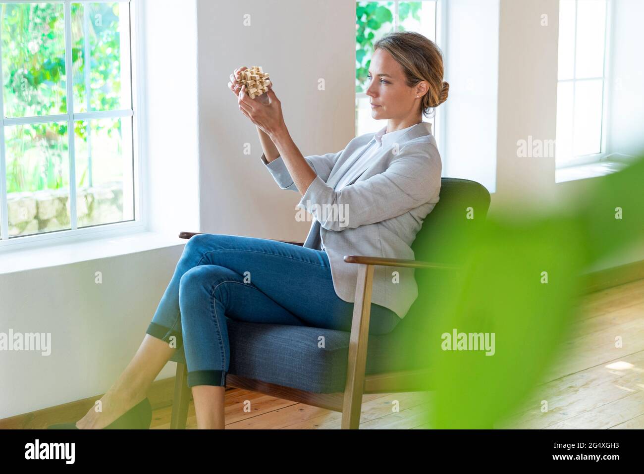 Donna imprenditore che tiene un oggetto di legno mentre si siede su una poltrona in ufficio Foto Stock