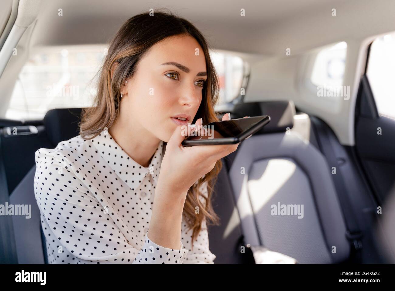 Donna d'affari che invia messaggi vocali tramite smartphone mentre si è seduti in auto Foto Stock