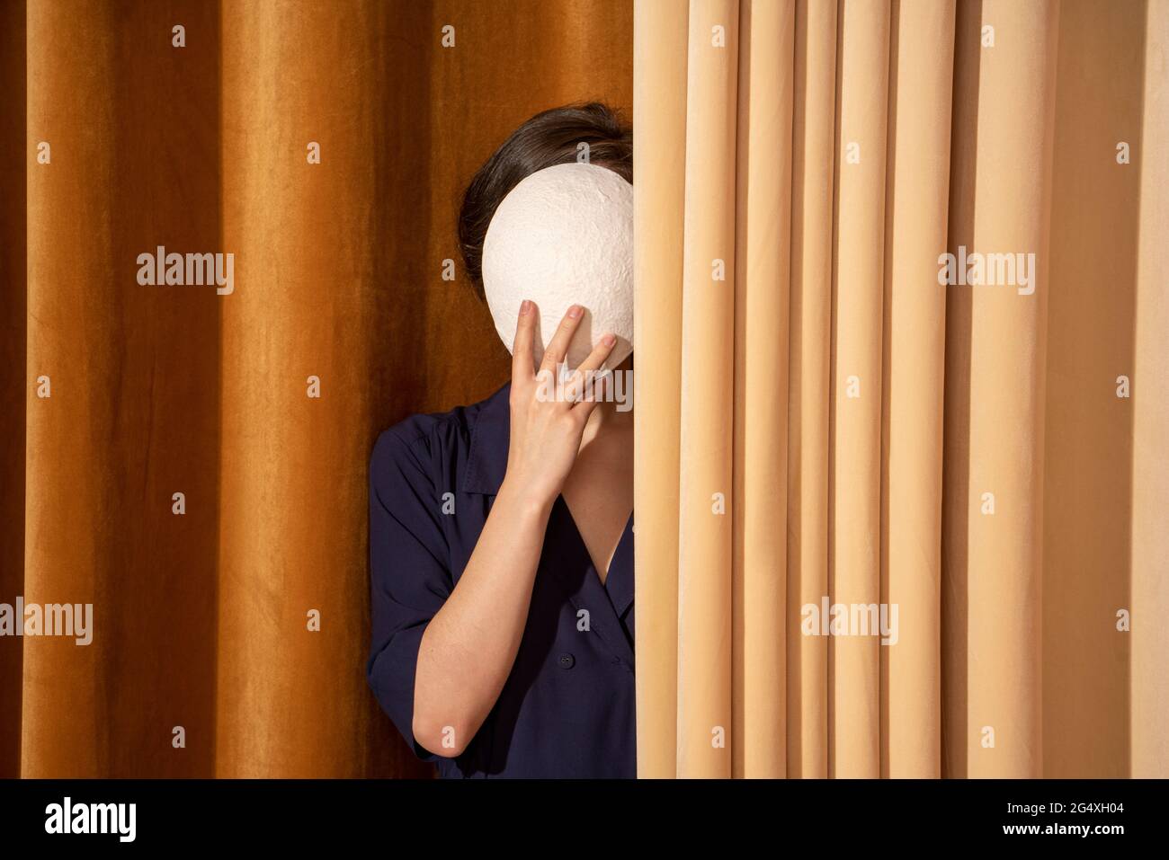 Donna che copre il viso con maschera bianca da tenda Foto Stock